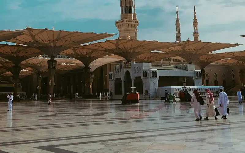 The courtyard of Masjid an-Nabawi in Madinah with its shade canopies open and pilgrims walking at sunrise