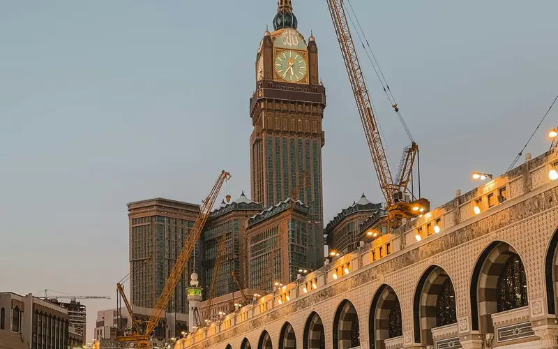The Makkah Royal Clock Tower above the illuminated arcade of Masjid al-Haram at dusk