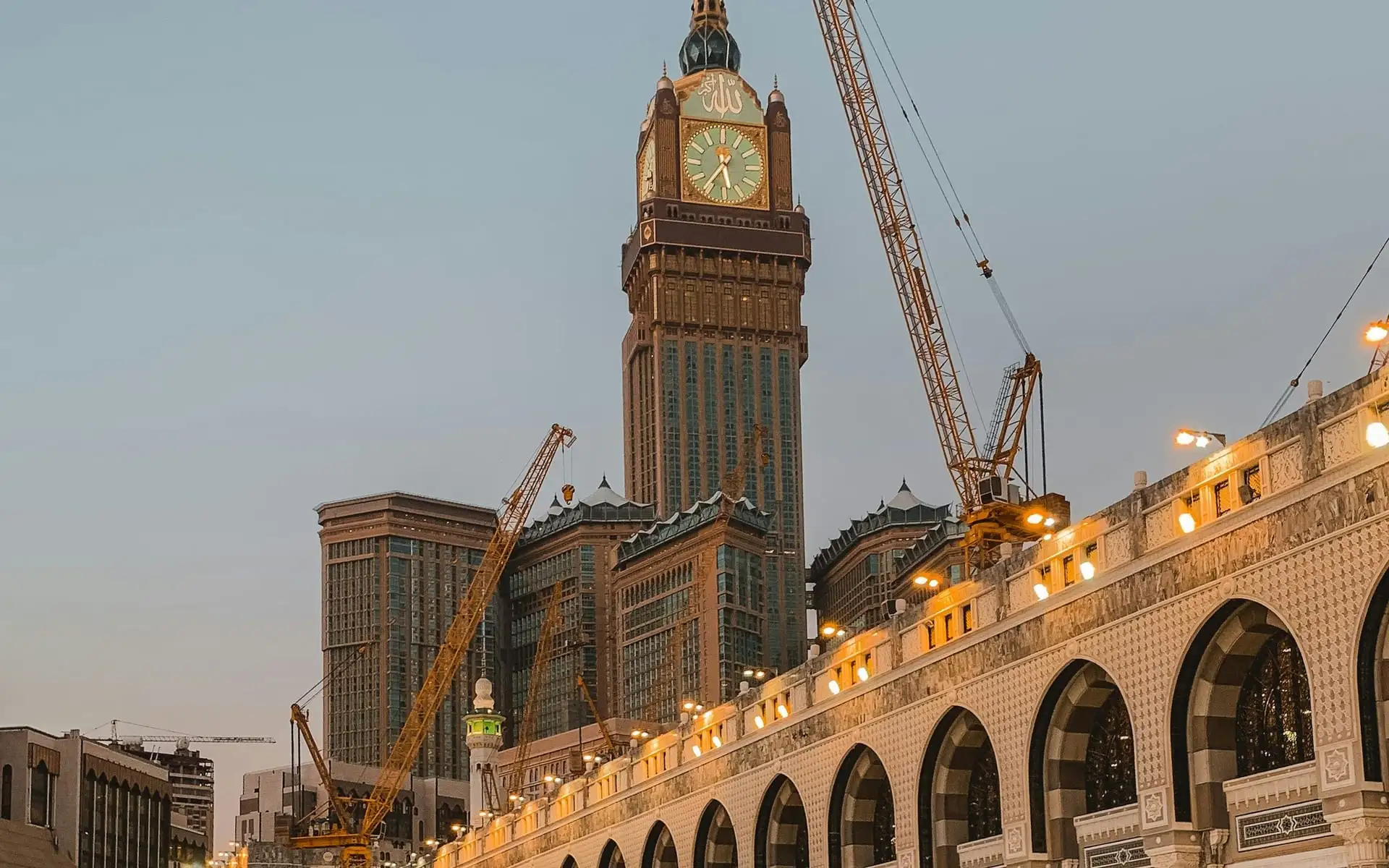 The Makkah Royal Clock Tower above the illuminated arcade of Masjid al-Haram at dusk